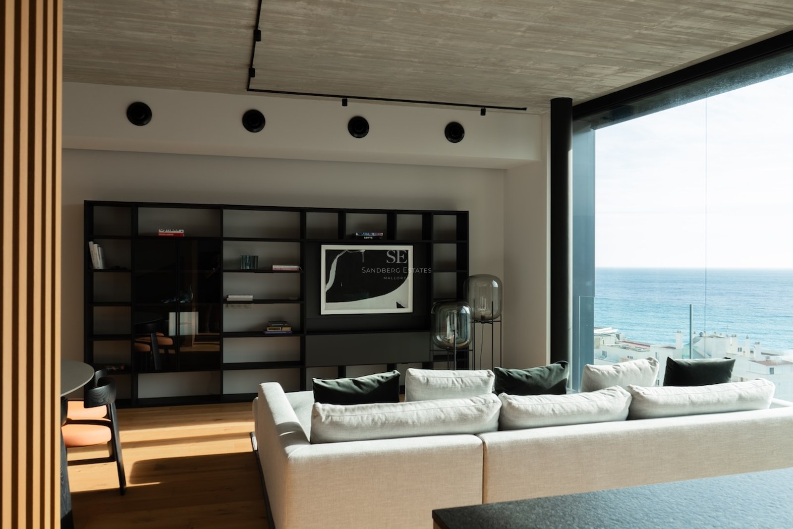 Zeitgenössisches Wohnzimmer mit bodentiefen Fenstern zum Meer, Eichenparkett und einem eleganten schwarzen Regal.