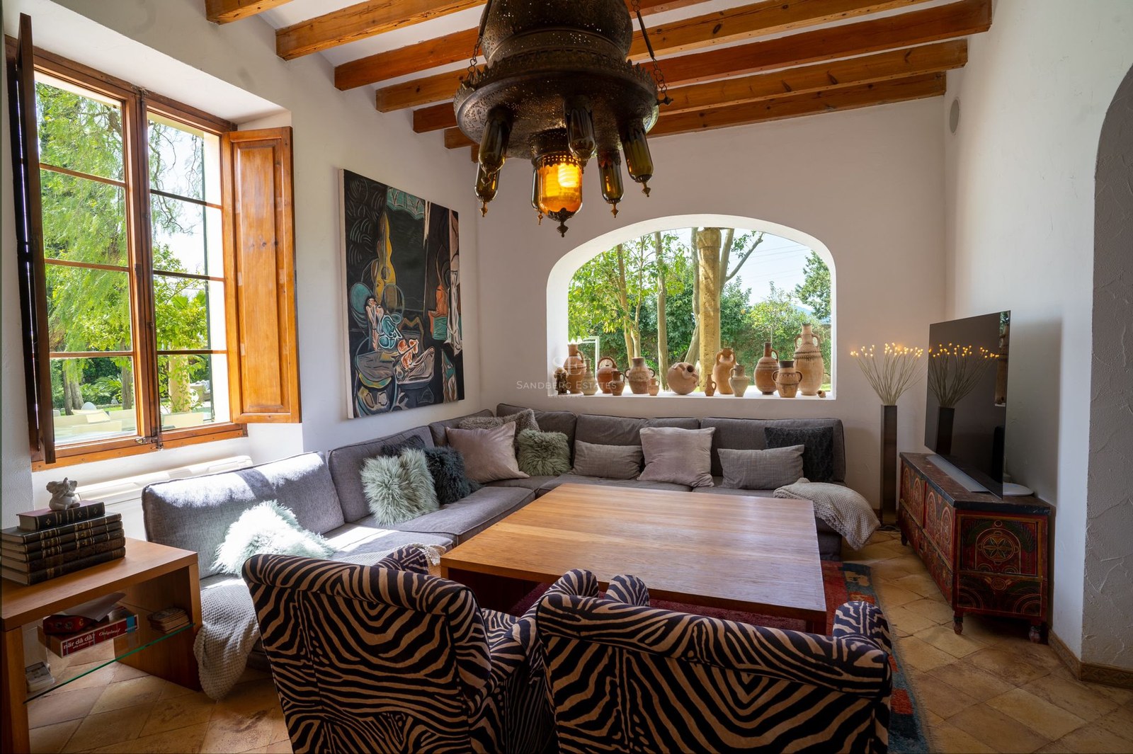 Salón acogedor con vigas de madera vistas, ventana en arco, sofá rinconera y sillones con estampado de cebra.