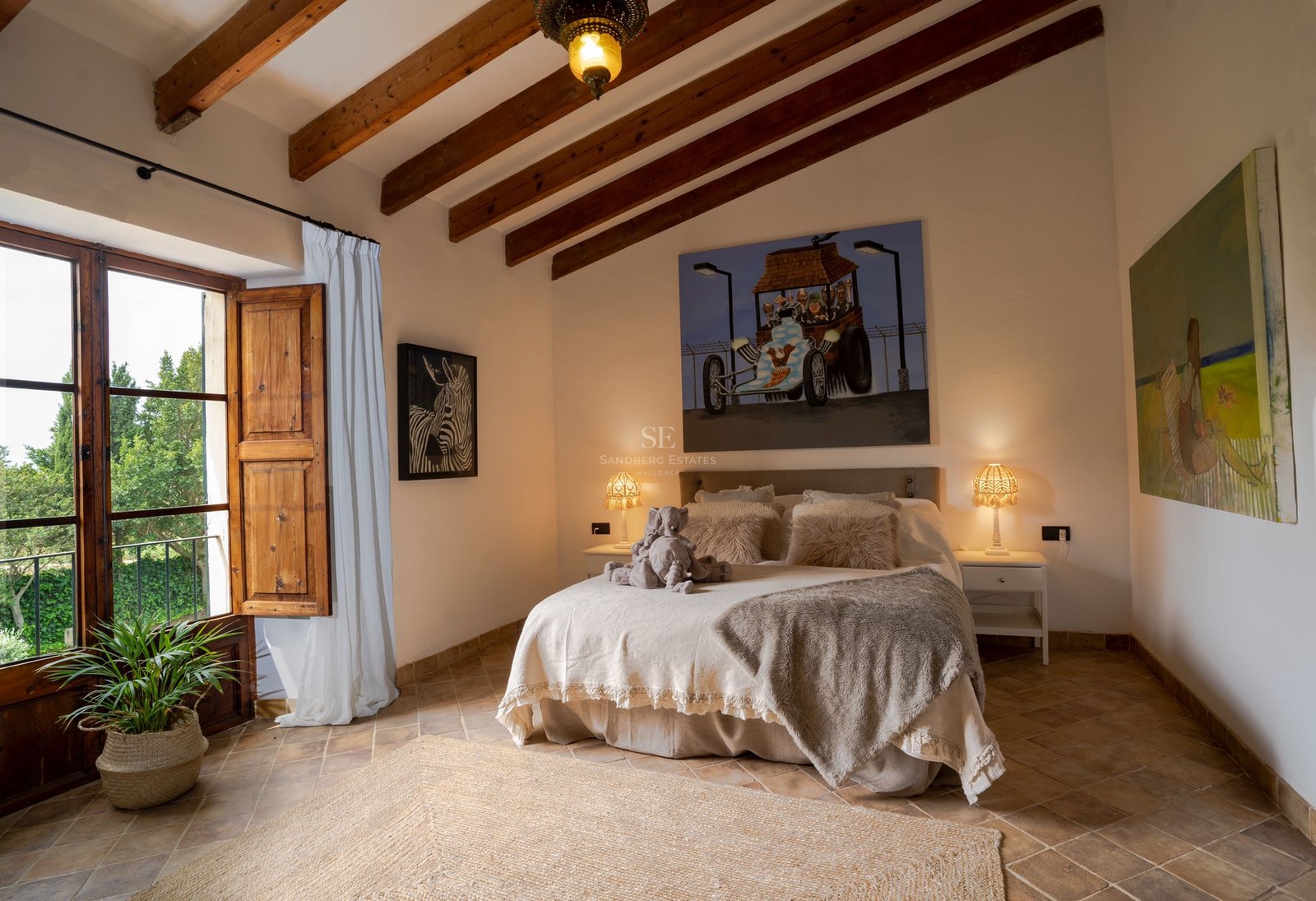 Dormitorio con vigas vistas de madera, suelo de terracota y cama doble con luz cálida y decoración acogedora.