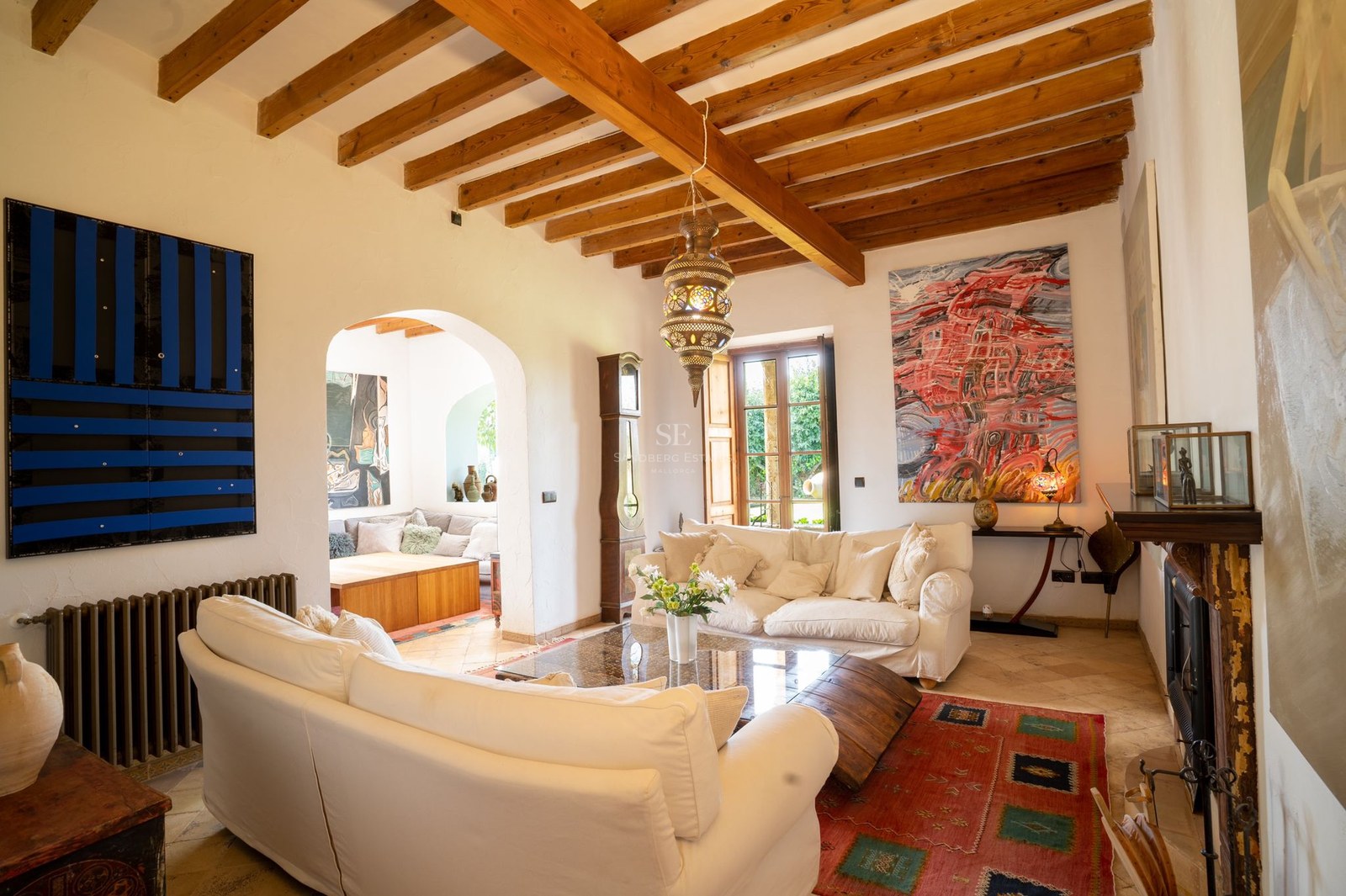 Salón con sofás blancos, techos altos de vigas de madera y una lámpara tradicional en una villa mediterránea.