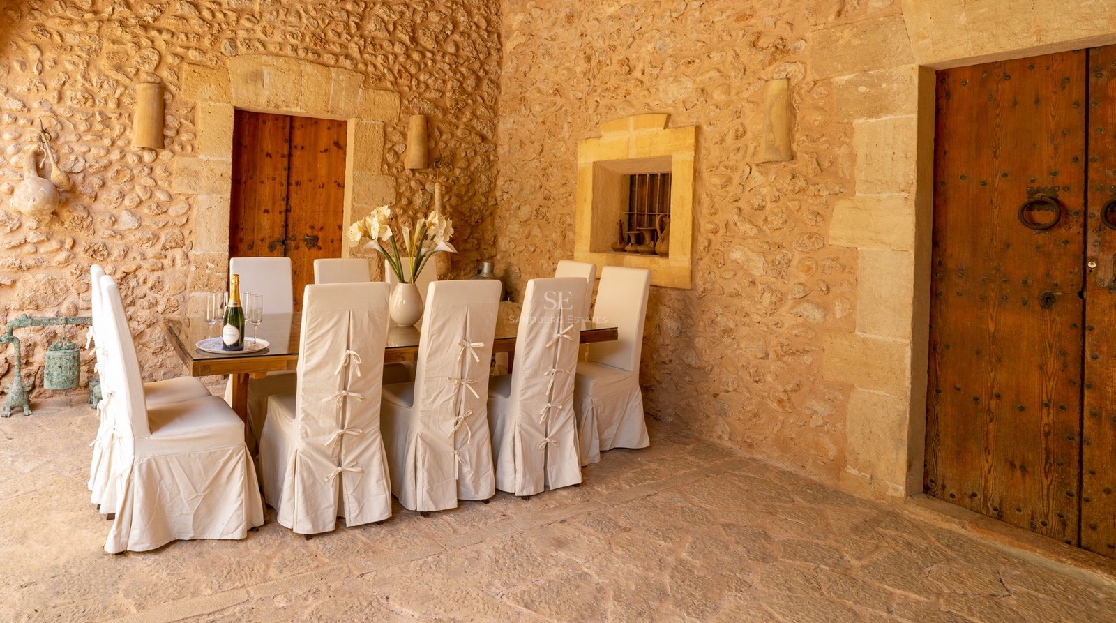 Comedor con paredes de piedra vista, mesa de madera y sillas con fundas de lino blanco.