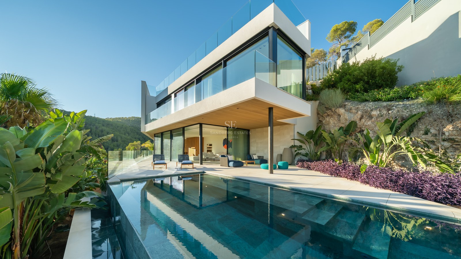 Panoramic view of a modern villa with an infinity pool, manicured lawn, and minimalist architectural design. Large windows and sunny terraces.