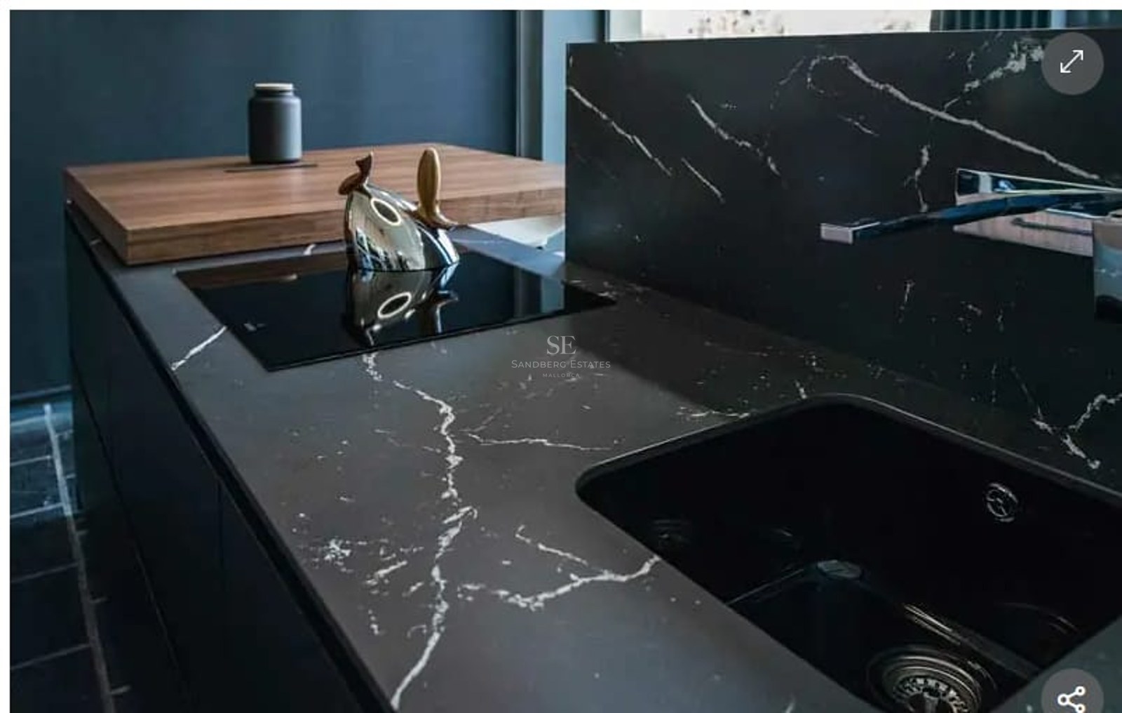 Close-up of a black marble kitchen island featuring an integrated sink, induction hob, and wooden breakfast bar.