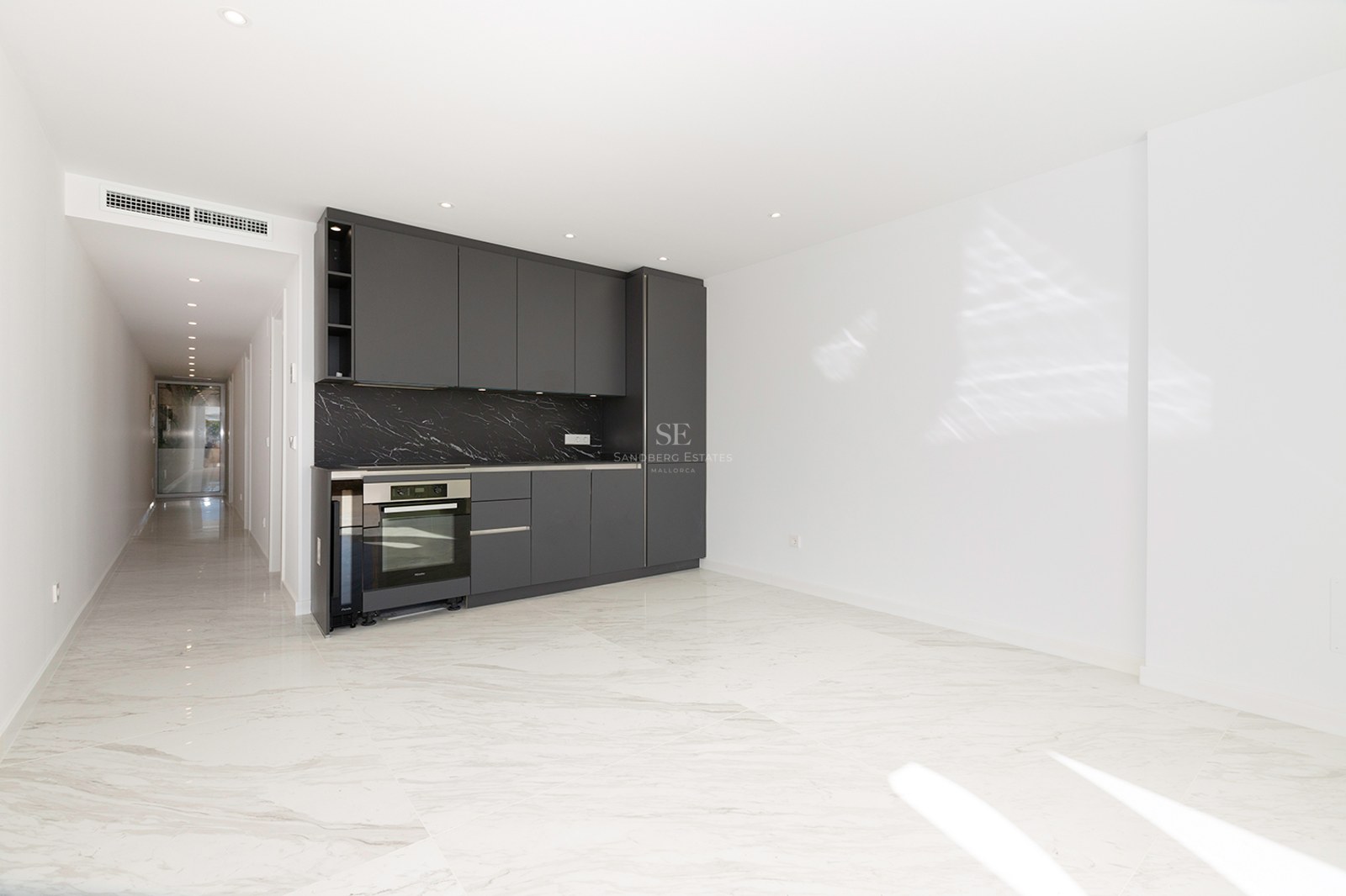 Modern kitchen area with dark gray cabinets, black marble backsplash, and white marble floors in a bright open room.