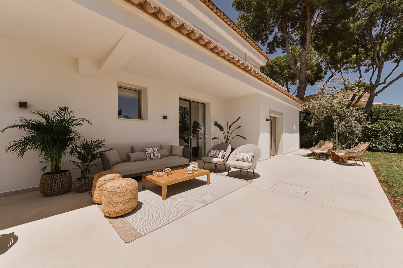 Terraza cubierta con sofá contemporáneo, mesa de madera y pufs de mimbre sobre suelos de piedra clara.
