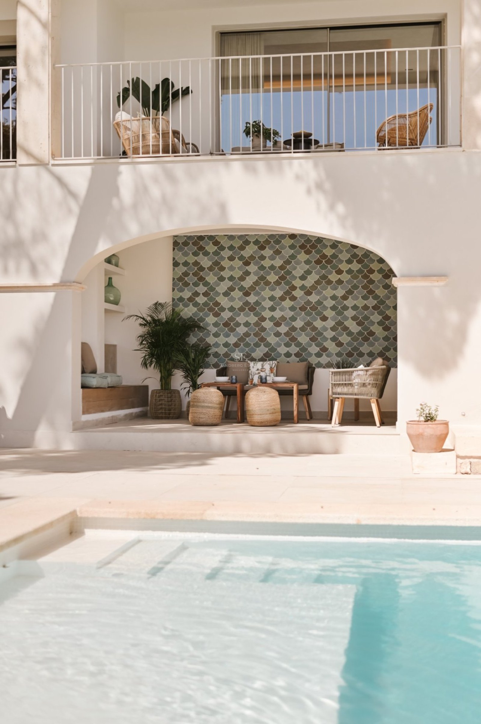 Piscina de lujo con escaleras integradas frente a una terraza cubierta con arcos y muebles de mimbre.