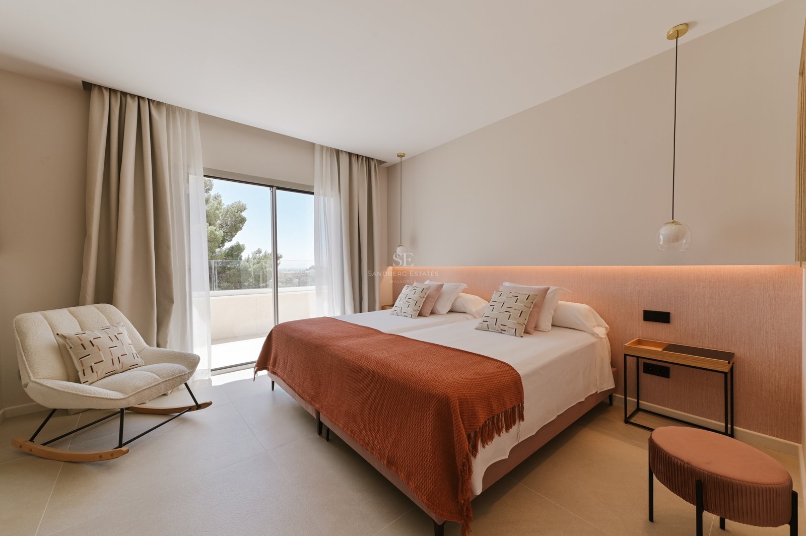 Dormitorio moderno con cama doble, manta terracota y ventanales de suelo a techo que dan a una terraza soleada.