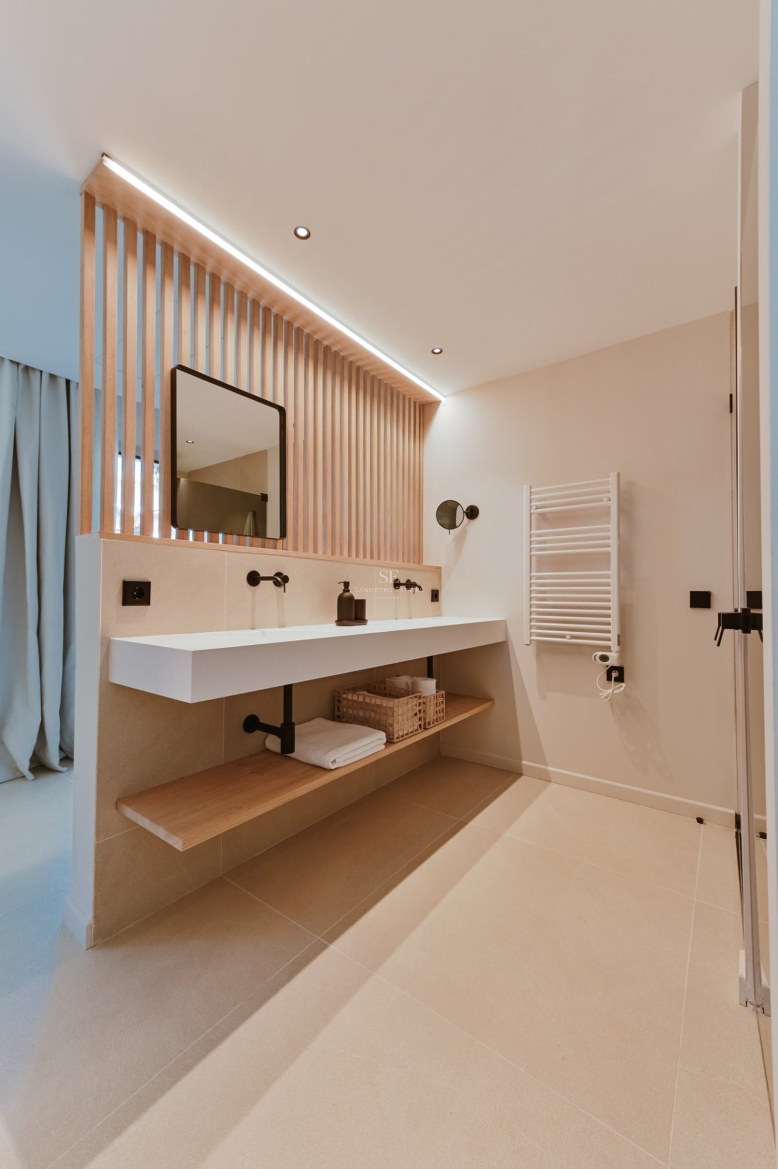 Baño moderno con lavabo suspendido blanco, grifería negra mate y panel de listones de madera verticales.