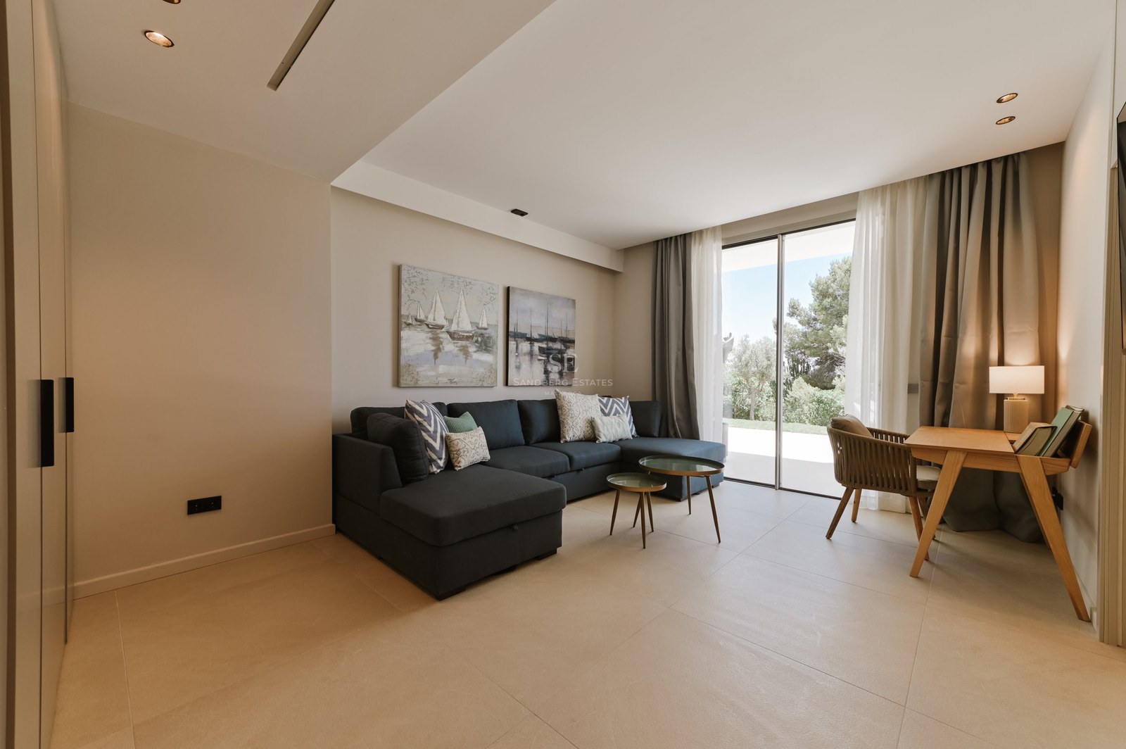 Salón moderno con sofá modular gris oscuro y ventanales de suelo a techo con vistas a la terraza.