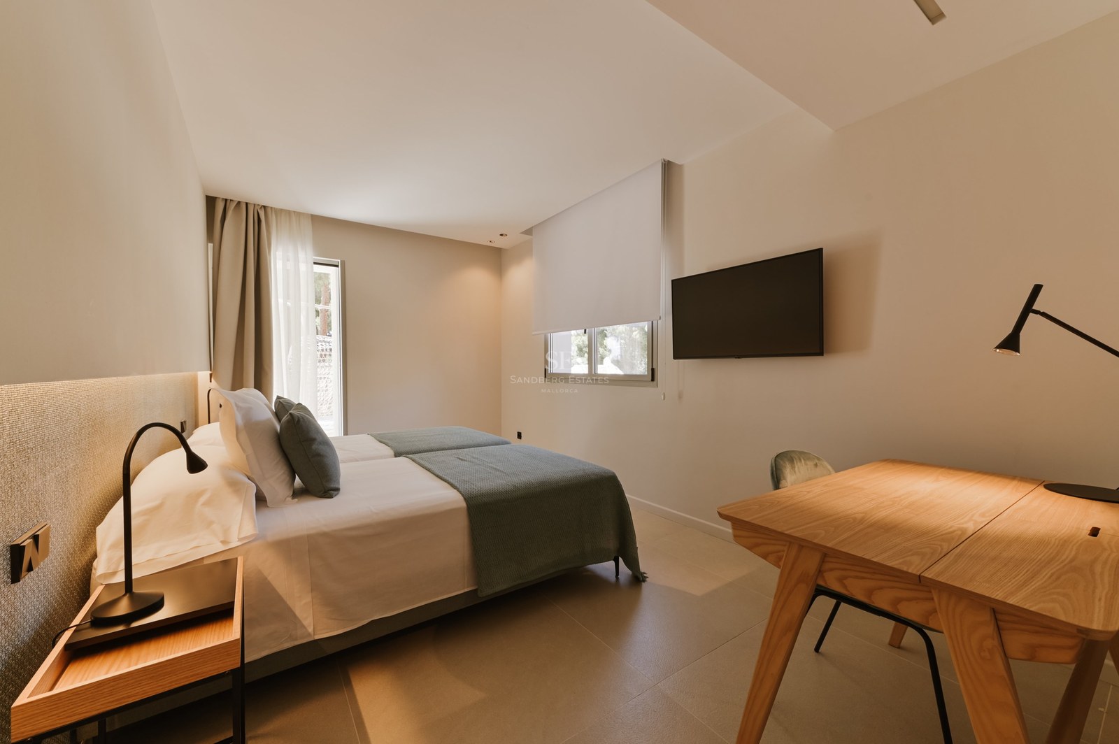 Dormitorio minimalista con camas gemelas, ropa de cama gris, escritorio de madera y televisor de pared.