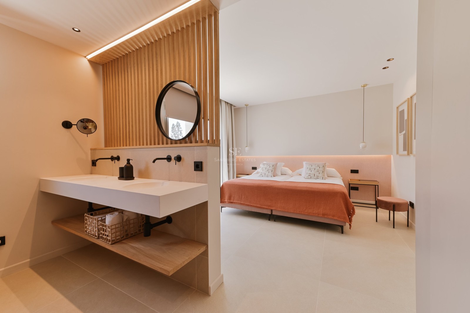 Dormitorio con separador de listones de madera entre el lavabo doble y una cama con textiles terracota.
