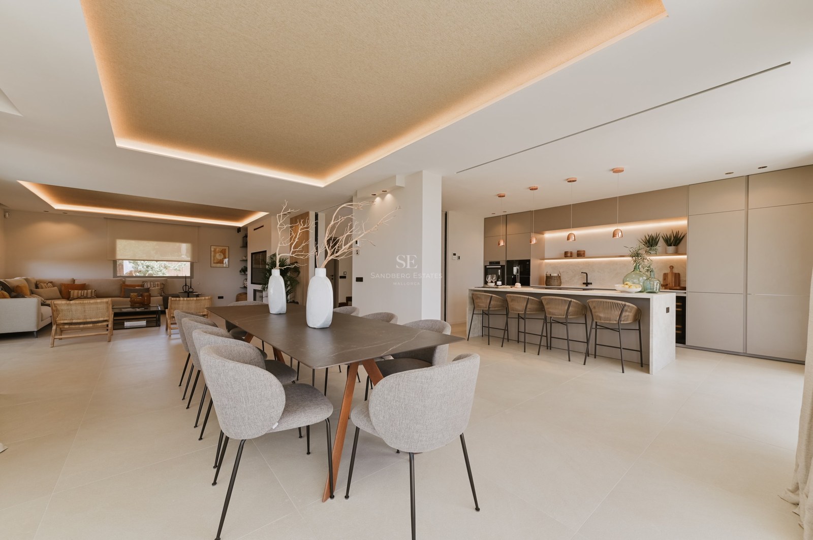 Comedor moderno con mesa larga, sillas tapizadas grises y cocina minimalista con iluminación LED indirecta.