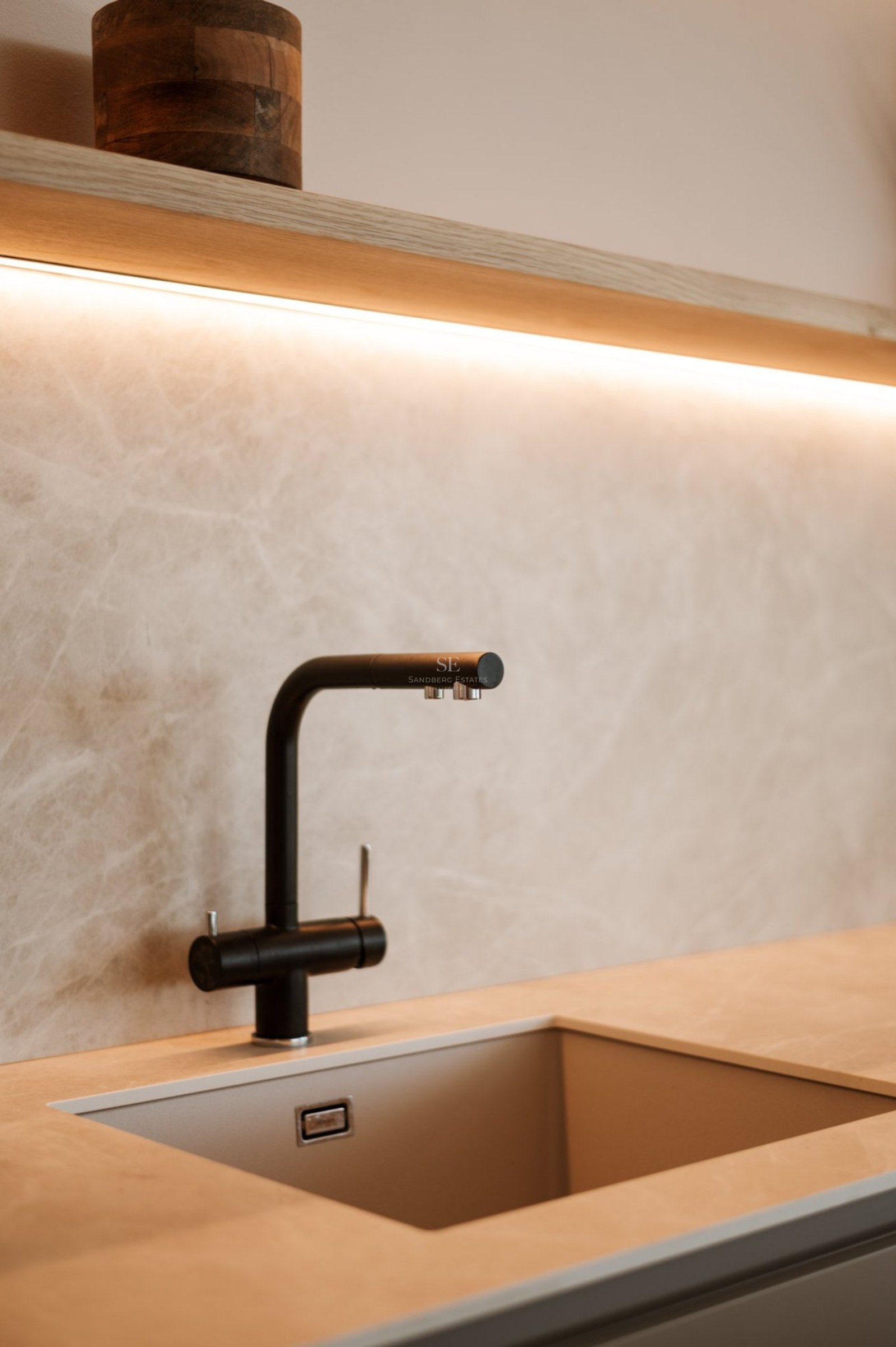 Grifo negro mate sobre salpicadero de piedra beige con iluminación LED integrada en una cocina de lujo.