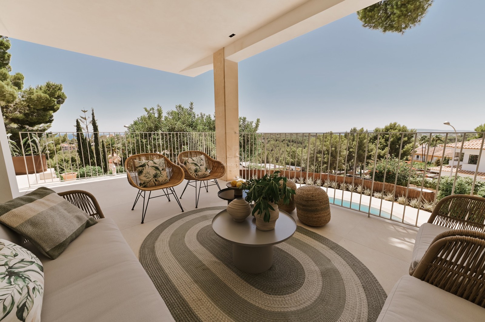 Terraza de piedra cubierta con sillones de mimbre, alfombra ovalada y mesa redonda con vistas a un parque y piscina.