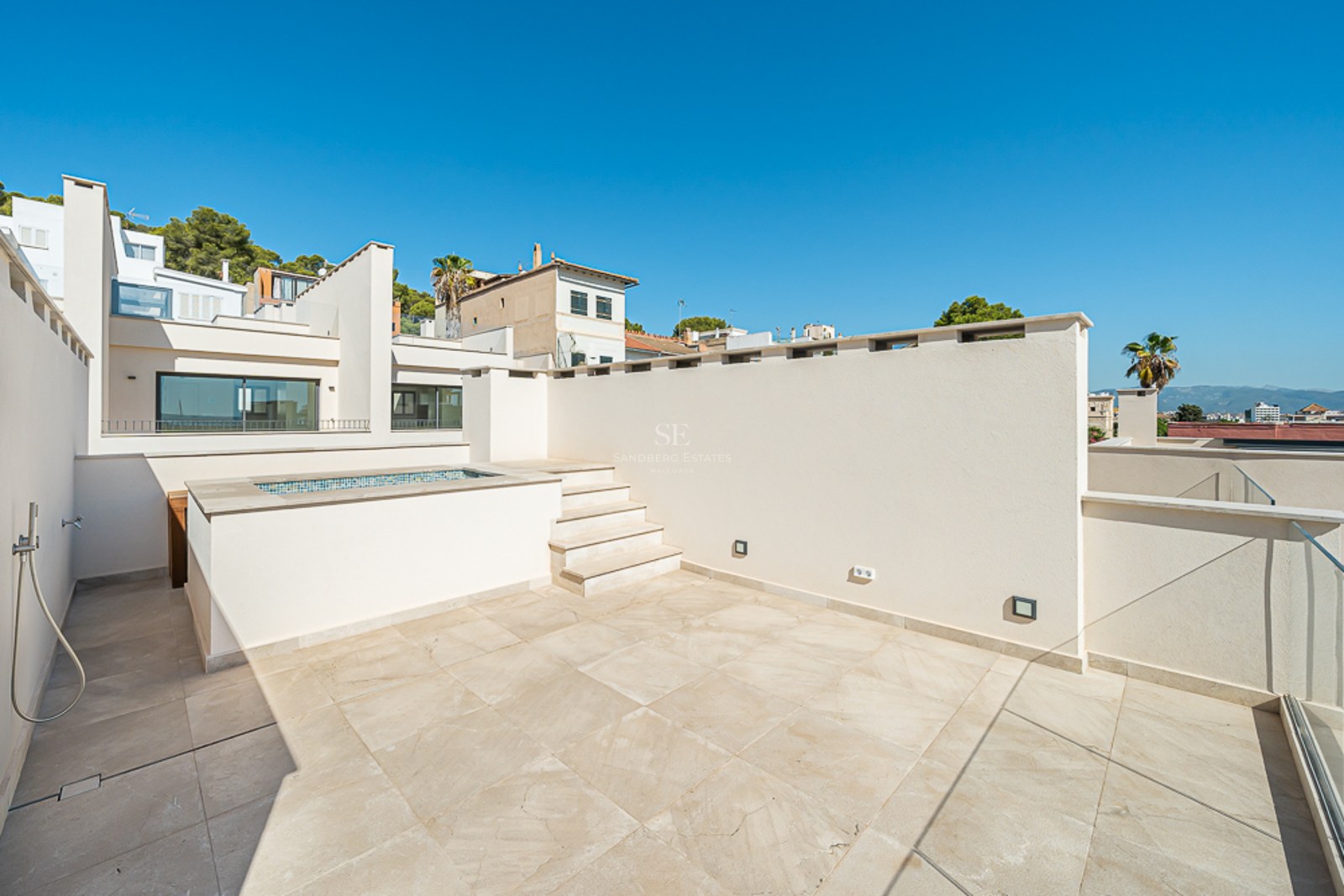 Terraza en azotea con suelo de piedra clara, pequeña piscina elevada, barandillas de cristal y ducha exterior.