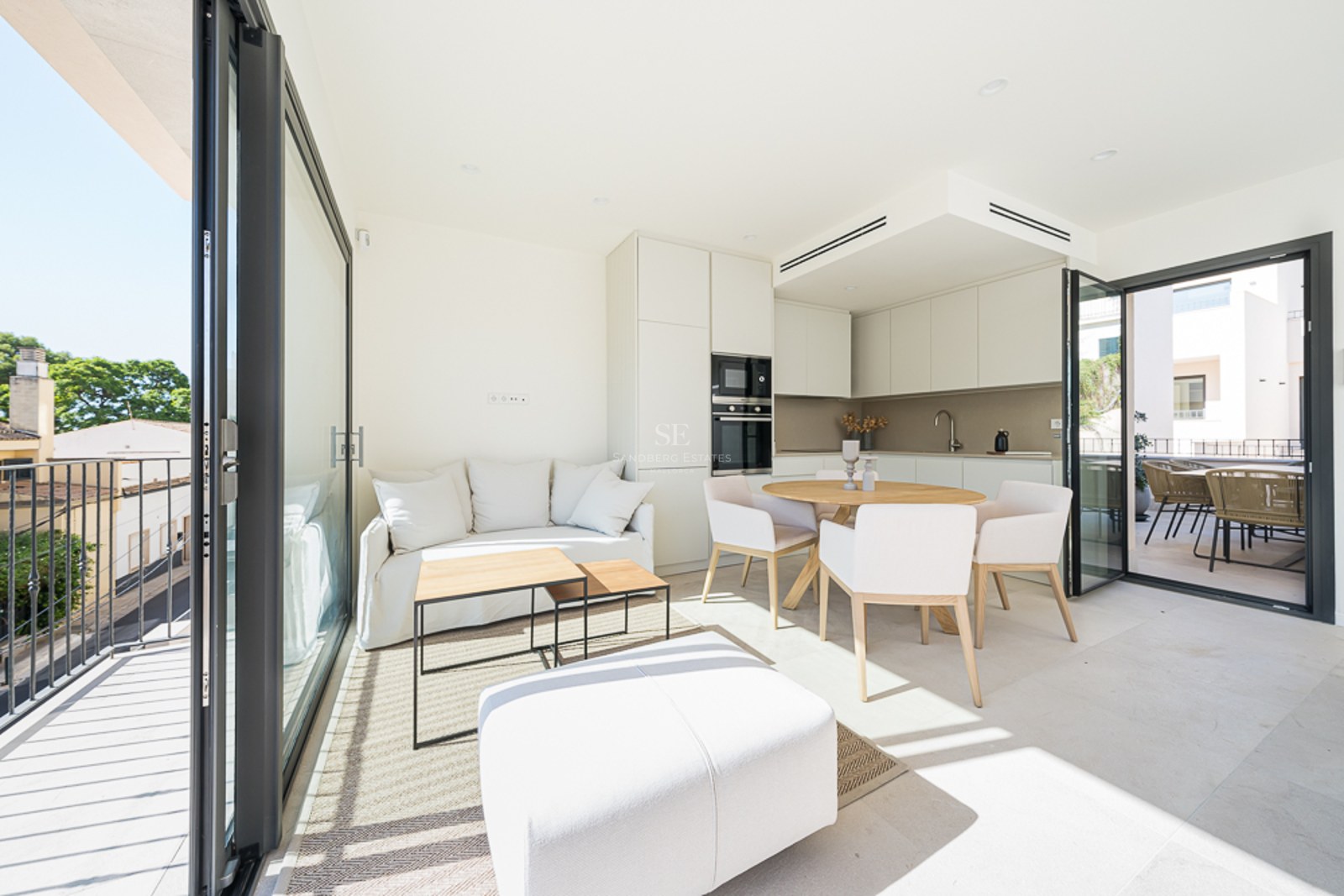 Salón y comedor luminoso de planta abierta con muebles blancos, detalles en madera y grandes ventanales a la terraza.