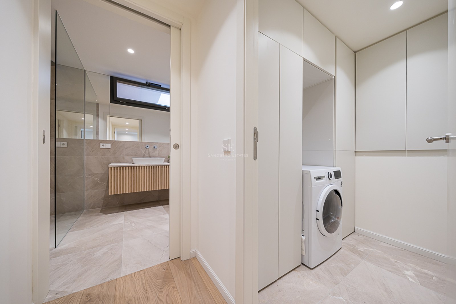 Zona de lavandería moderna con lavadora blanca y armarios empotrados junto a un baño de piedra con lavabo de diseño.