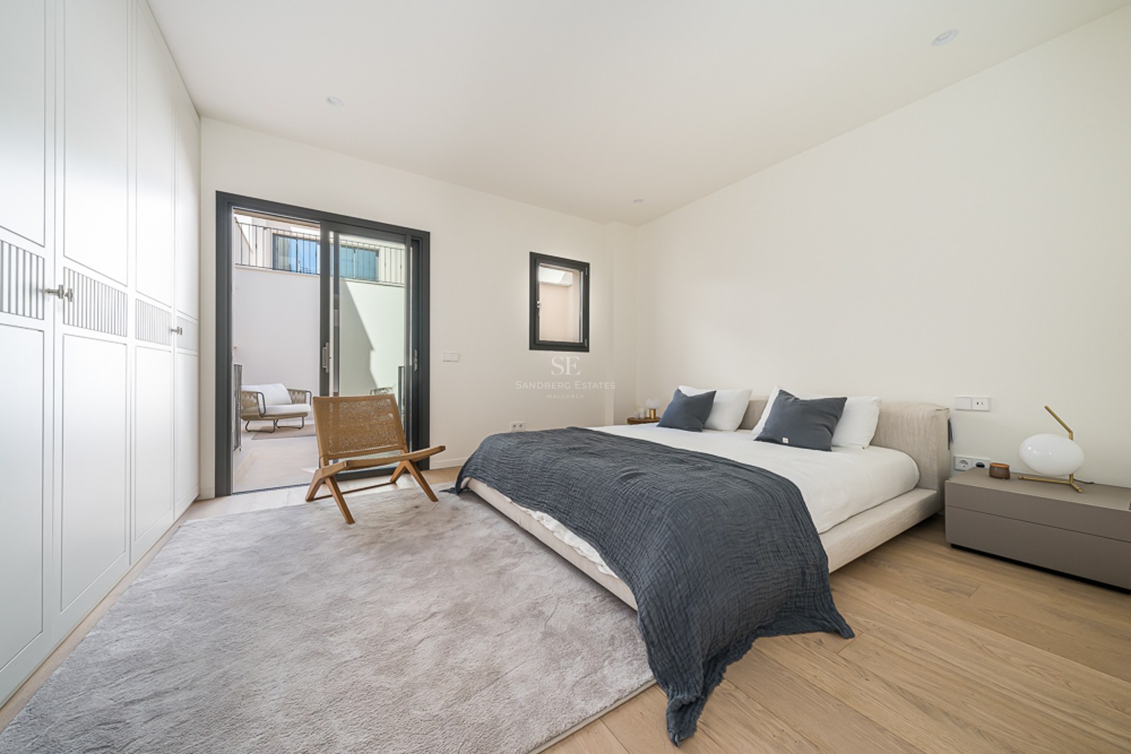 Dormitorio principal con armarios empotrados blancos, suelo de roble y acceso a terraza mediante puerta corredera.