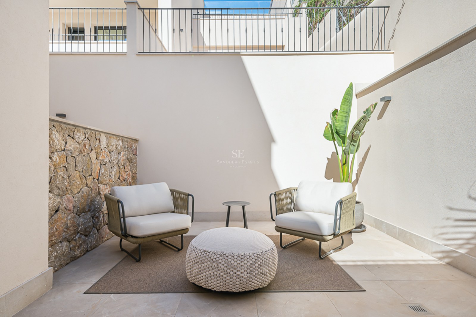 Patio cerrado con dos sillones, puf de punto, muro de piedra natural y una planta ave del paraíso.