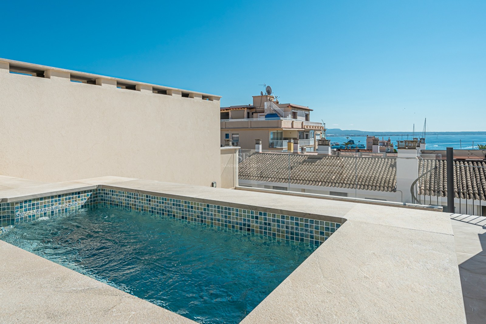 Moderna piscina en azotea rodeada de piedra natural con vistas a los tejados de la ciudad y al mar Mediterráneo.