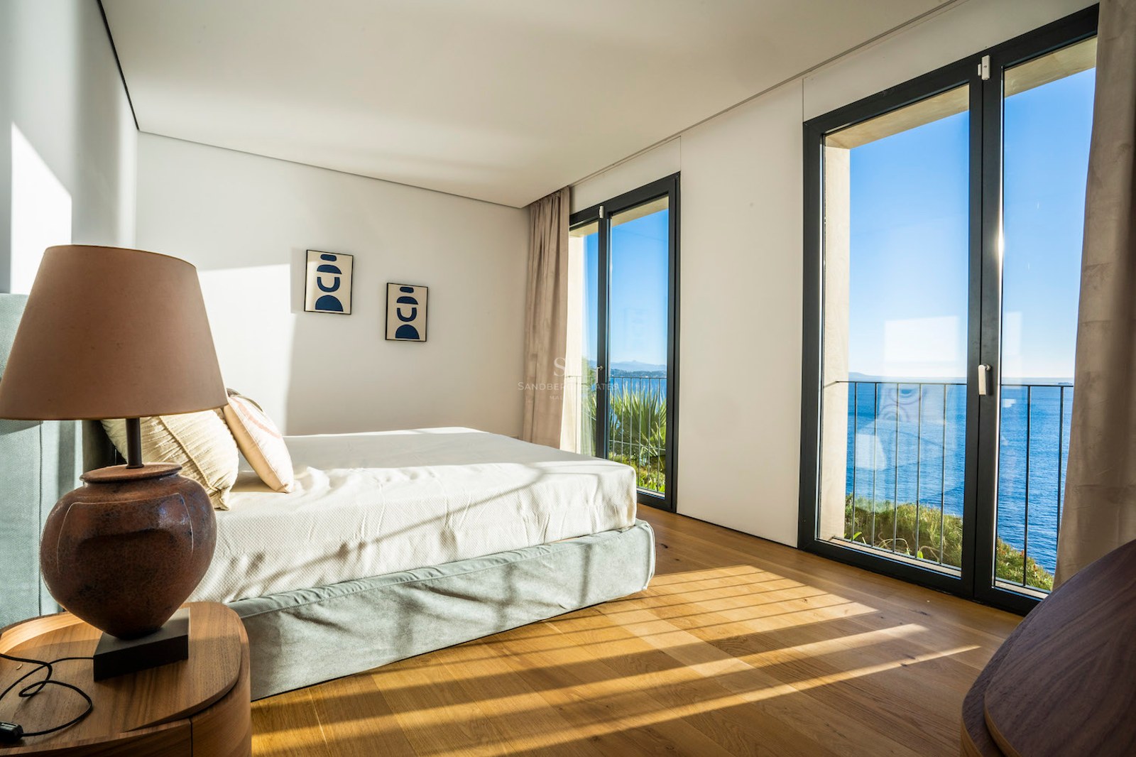 Modern master bedroom featuring oak flooring, floor-to-ceiling windows, and a view of the blue Mediterranean sea.