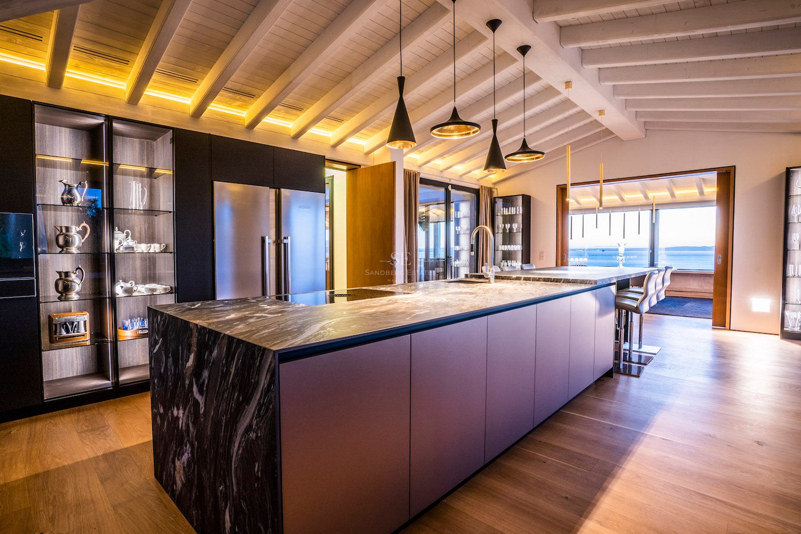 Modern kitchen featuring a large marble island, dark cabinetry, wood beamed ceilings, and a sea view.