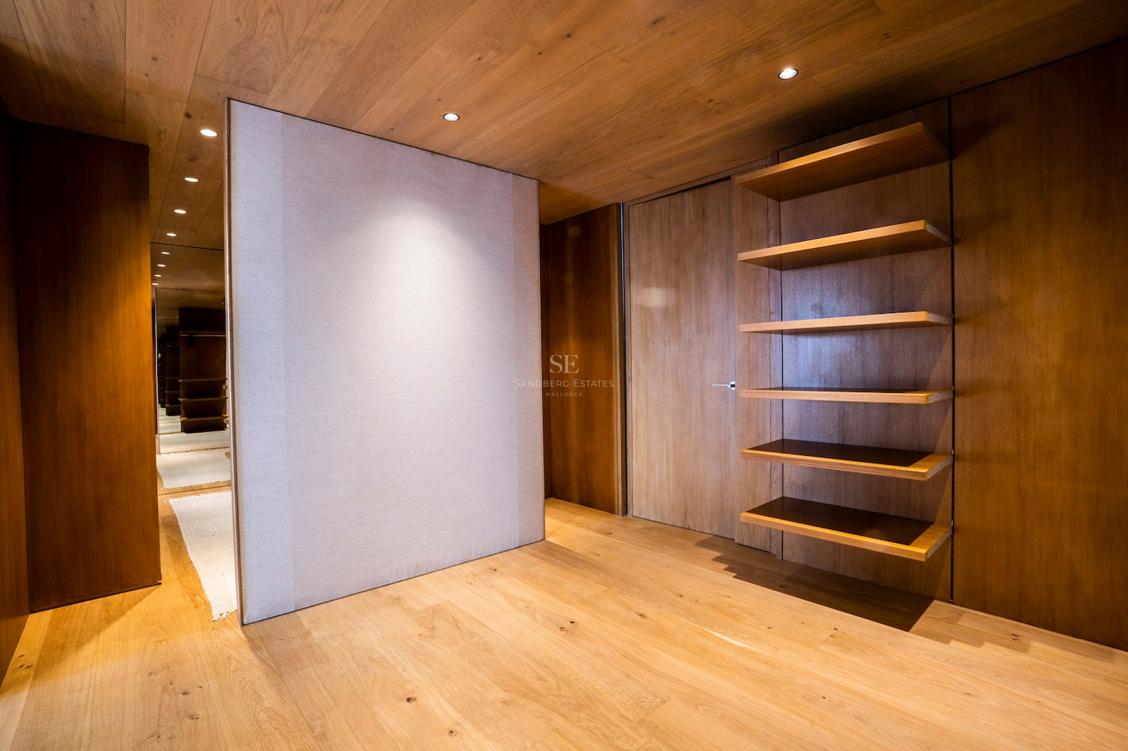 Minimalist dressing room with natural oak wood walls, ceiling, and floor, featuring built-in shelves and warm lighting.