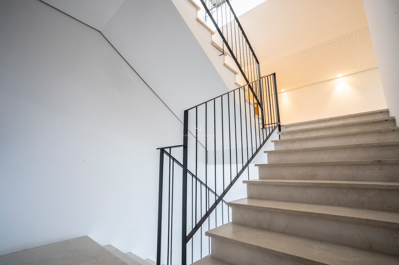 Cream marble staircase with black iron railing against white walls under soft natural light.