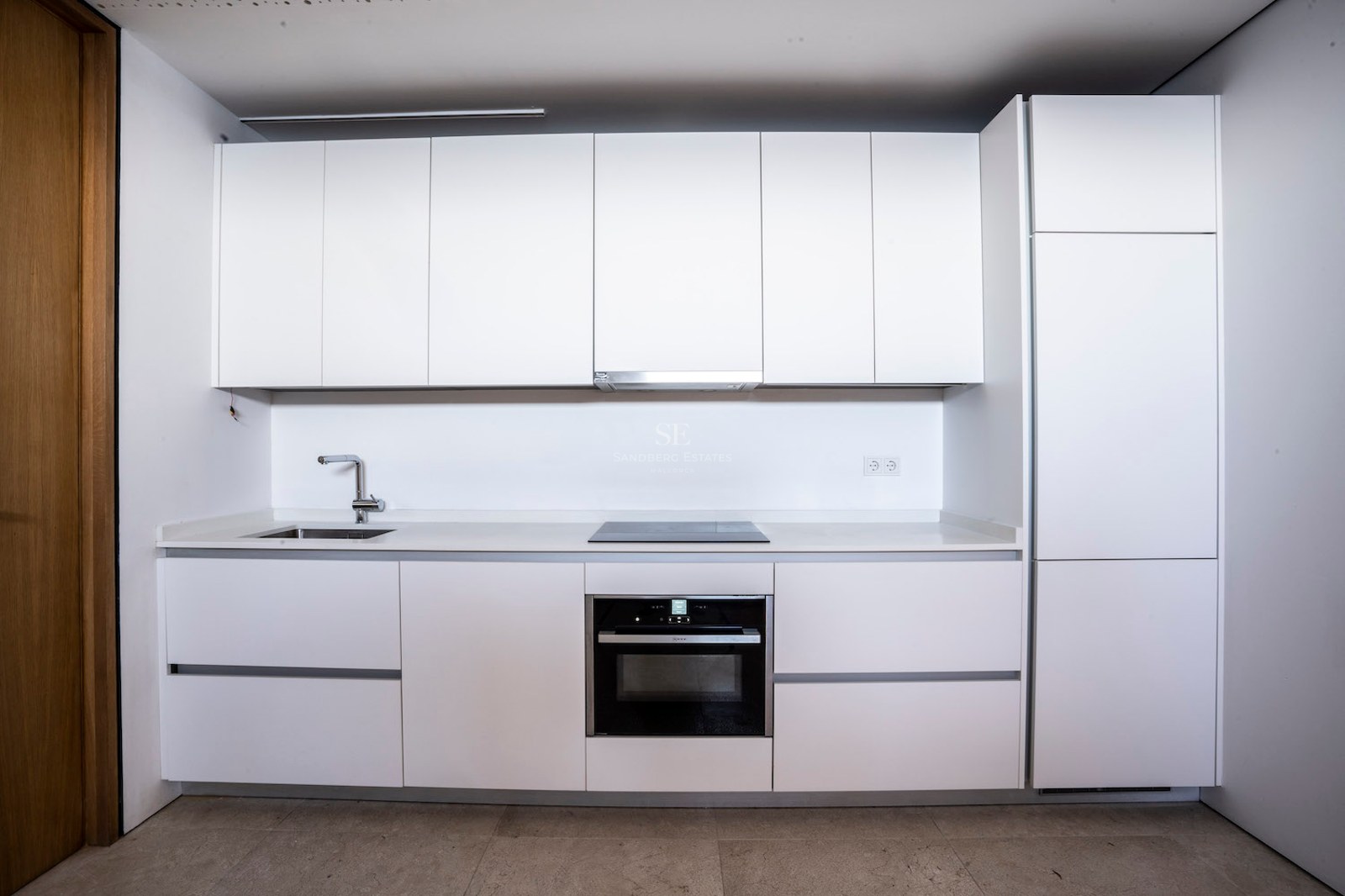 Modern white kitchen with handleless cabinetry, integrated oven, induction hob, and stainless steel sink.