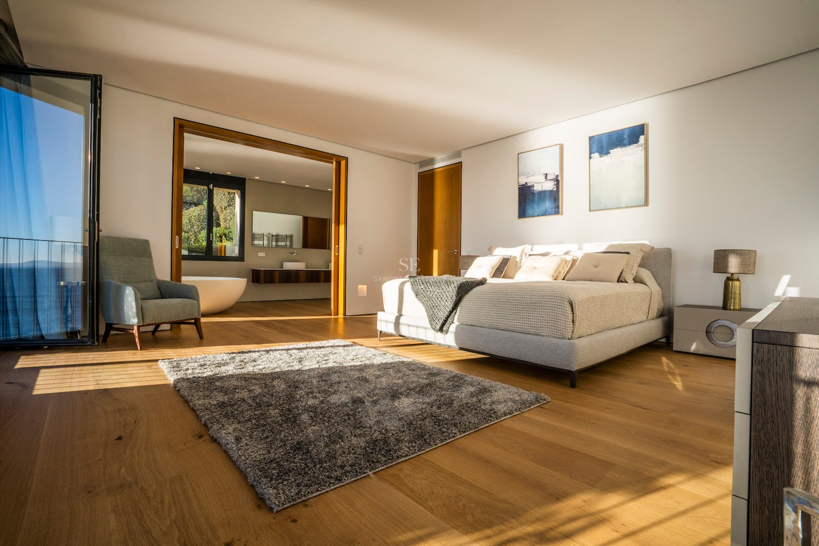 Modern master bedroom with oak floors, king-size bed, sea-view terrace access, and open-plan en-suite bathroom.