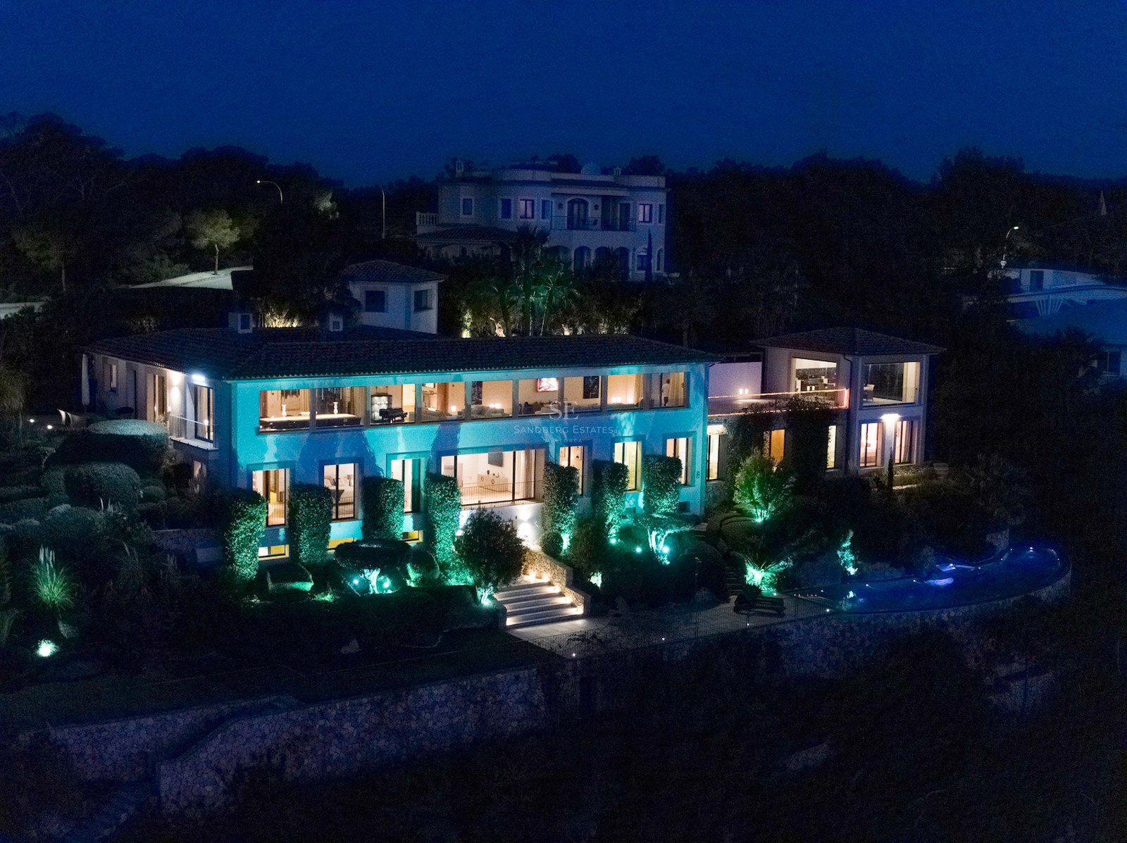 Night view of a two-story luxury villa featuring illuminated interiors, manicured gardens, and a private pool.