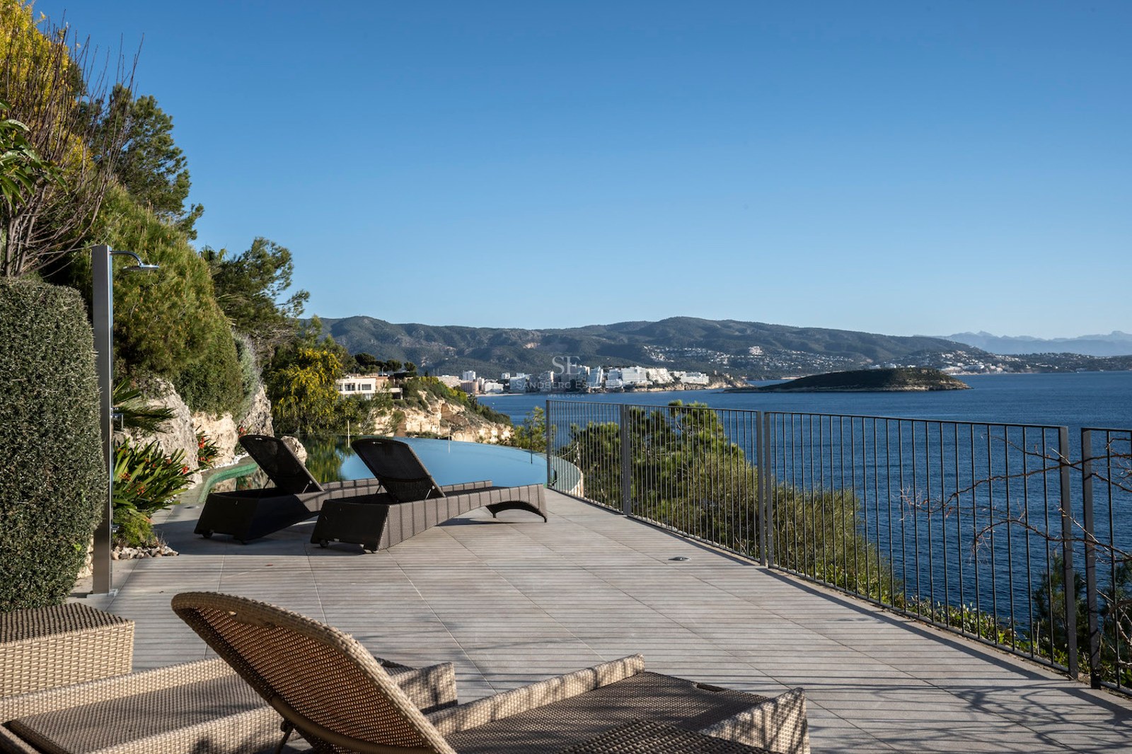 Luxury sun terrace with wicker loungers, infinity pool, and panoramic Mediterranean sea and mountain views.