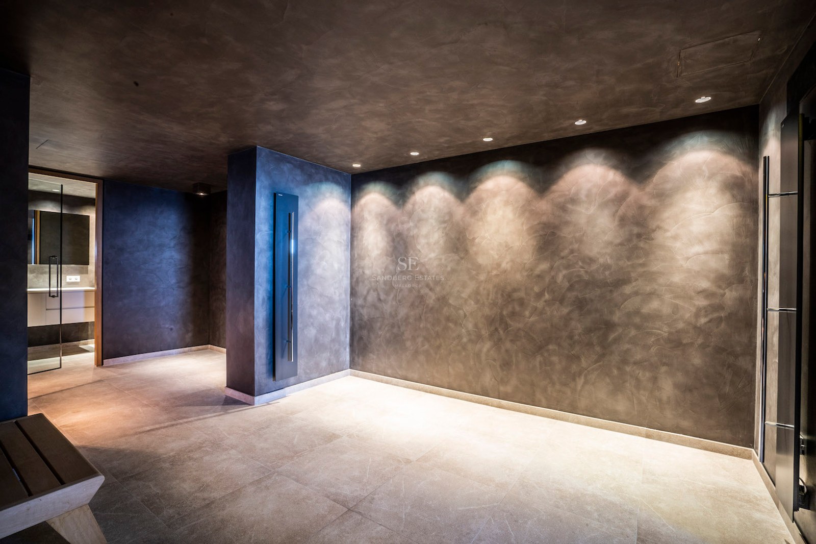 Minimalist spa area with dark textured plaster walls, recessed spotlighting, and light stone floor tiles.