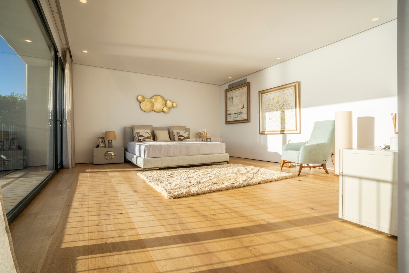 Bright modern master bedroom featuring oak floors, floor-to-ceiling glass doors, and contemporary furniture.