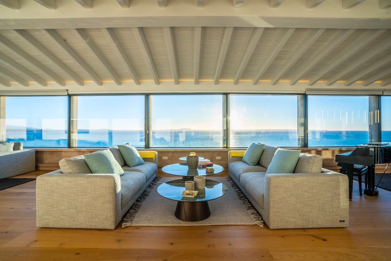 Modern living room featuring grey sofas, glass coffee tables, and floor-to-ceiling windows overlooking the Mediterranean.