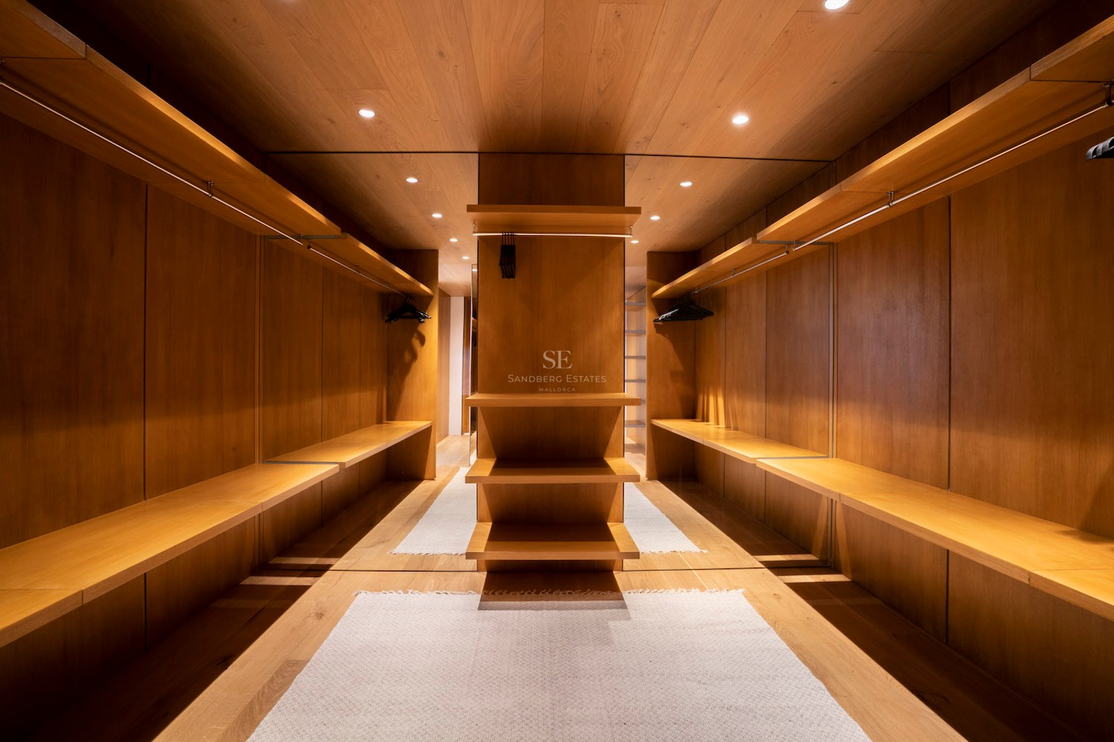 Symmetrical walk-in closet with floor-to-ceiling oak wood paneling, open shelving, and integrated warm lighting.