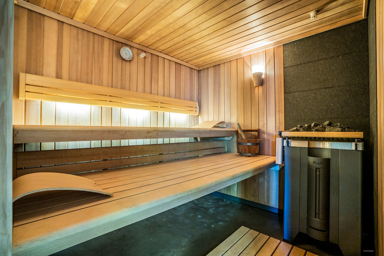Interior of a modern wooden sauna with multi-level benches, ambient lighting, and a professional KLAFS heater.