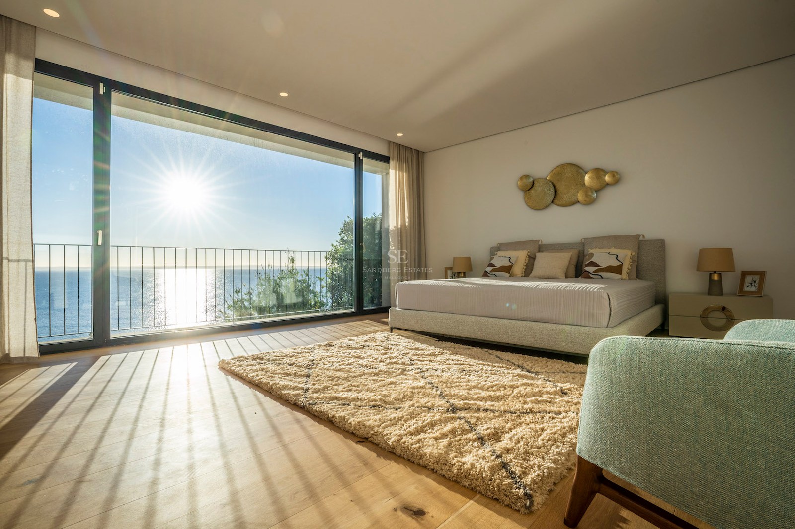 Bright master bedroom featuring floor-to-ceiling glass doors, oak flooring, and a terrace overlooking the blue sea.