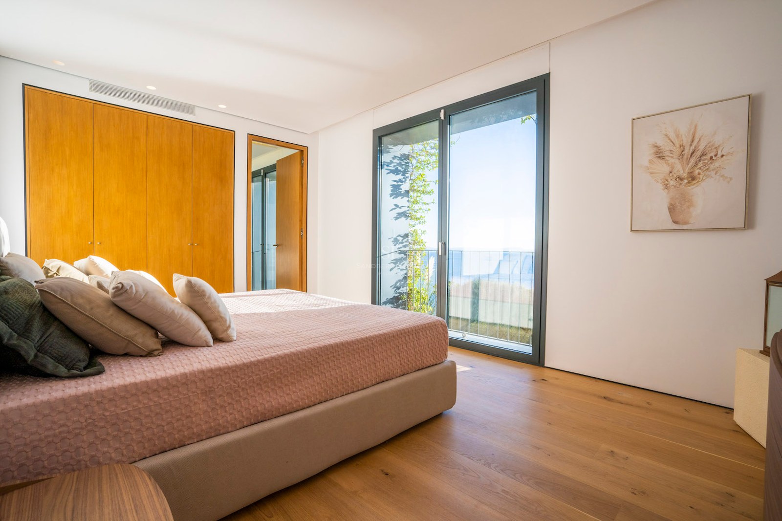 Bedroom featuring oak flooring, built-in wooden wardrobes, and floor-to-ceiling glass doors overlooking the sea.
