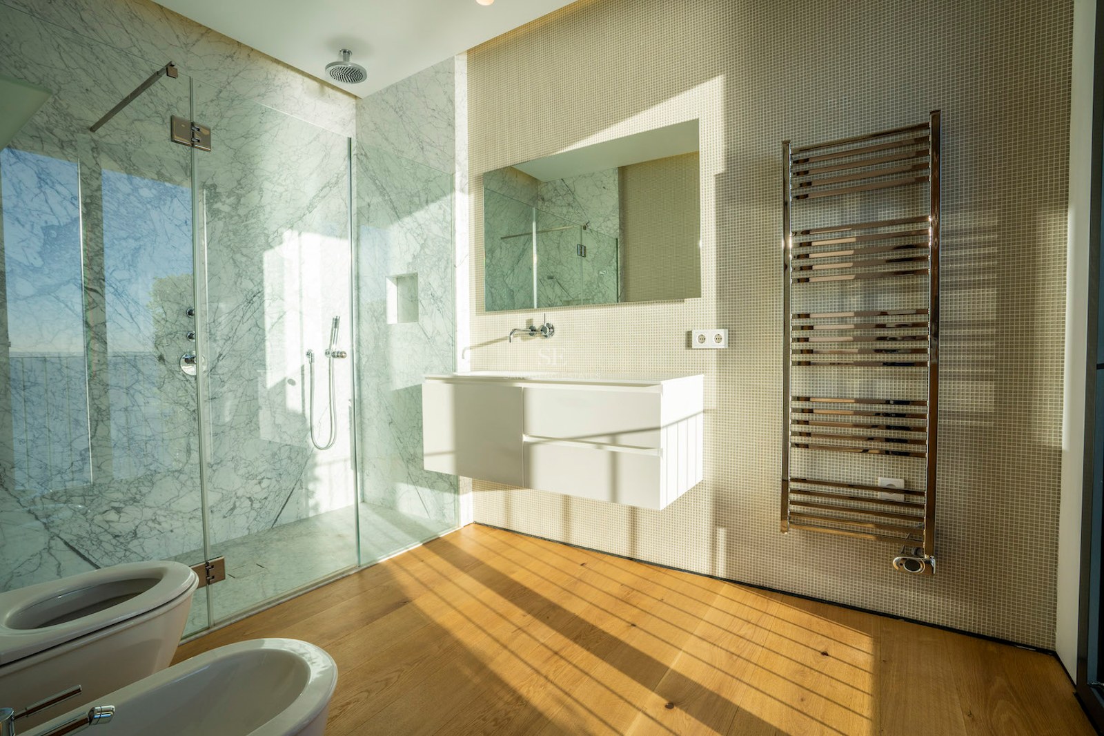 Contemporary bathroom featuring a glass walk-in shower with marble walls, floating white vanity, and oak flooring.