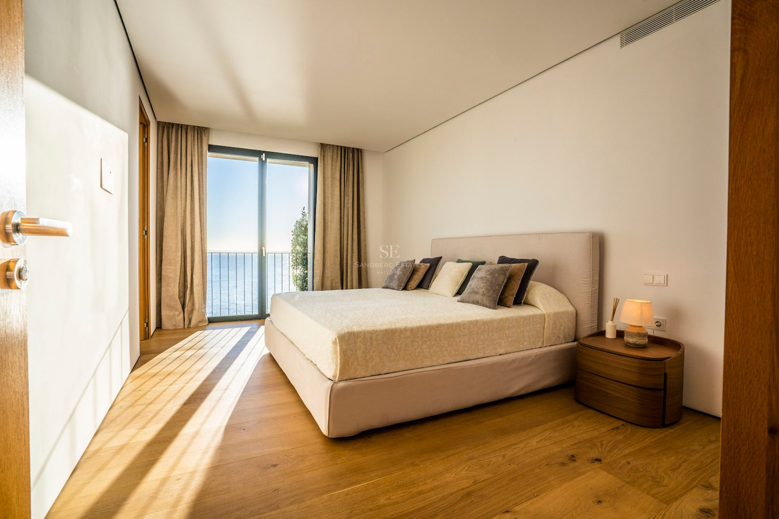 Modern bedroom featuring oak floors and floor-to-ceiling glass doors opening to a Mediterranean sea view.