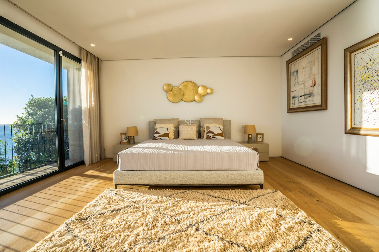 Modern master bedroom with oak floors, floor-to-ceiling glass doors opening to a terrace with sea views and natural light.