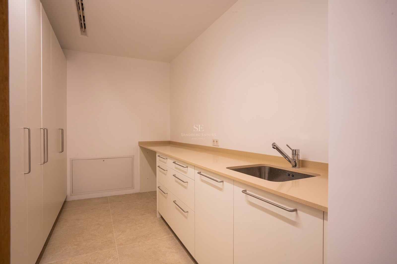 White utility room featuring a long beige countertop, stainless steel sink, and floor-to-ceiling storage cabinets.