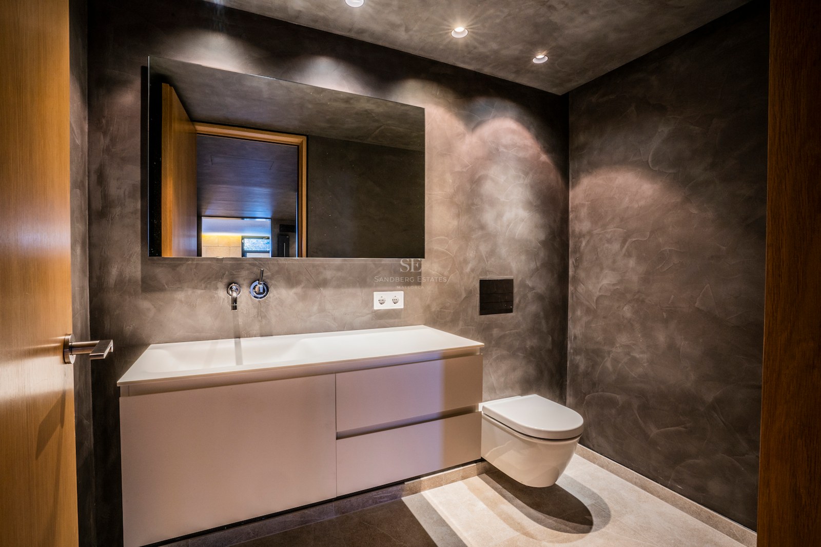 Contemporary bathroom featuring charcoal microcement walls, a white wall-hung vanity, and a large frameless mirror.