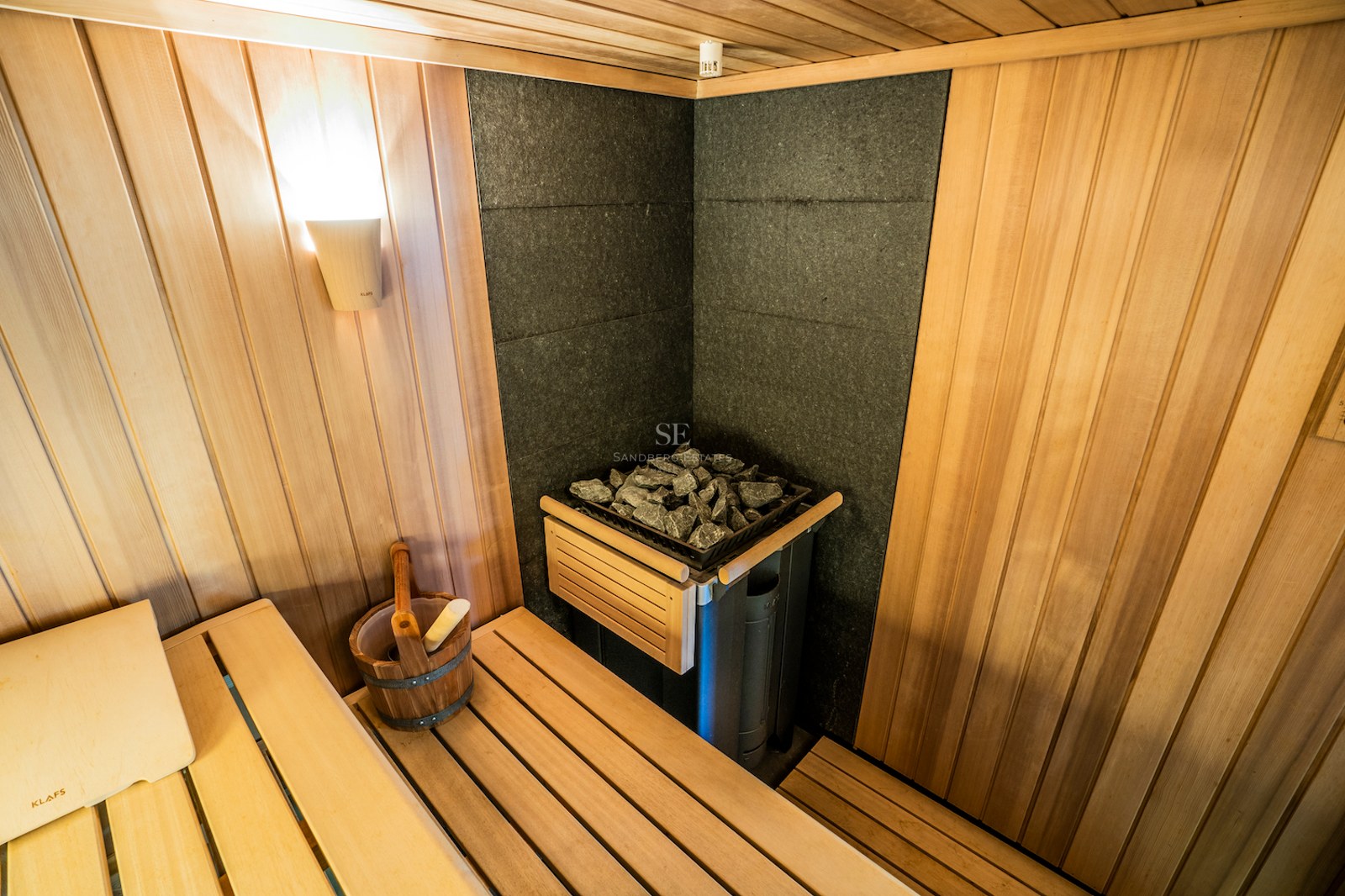 Interior of a wood-paneled sauna featuring a KLAFS stone heater, wooden bucket, and atmospheric lighting.
