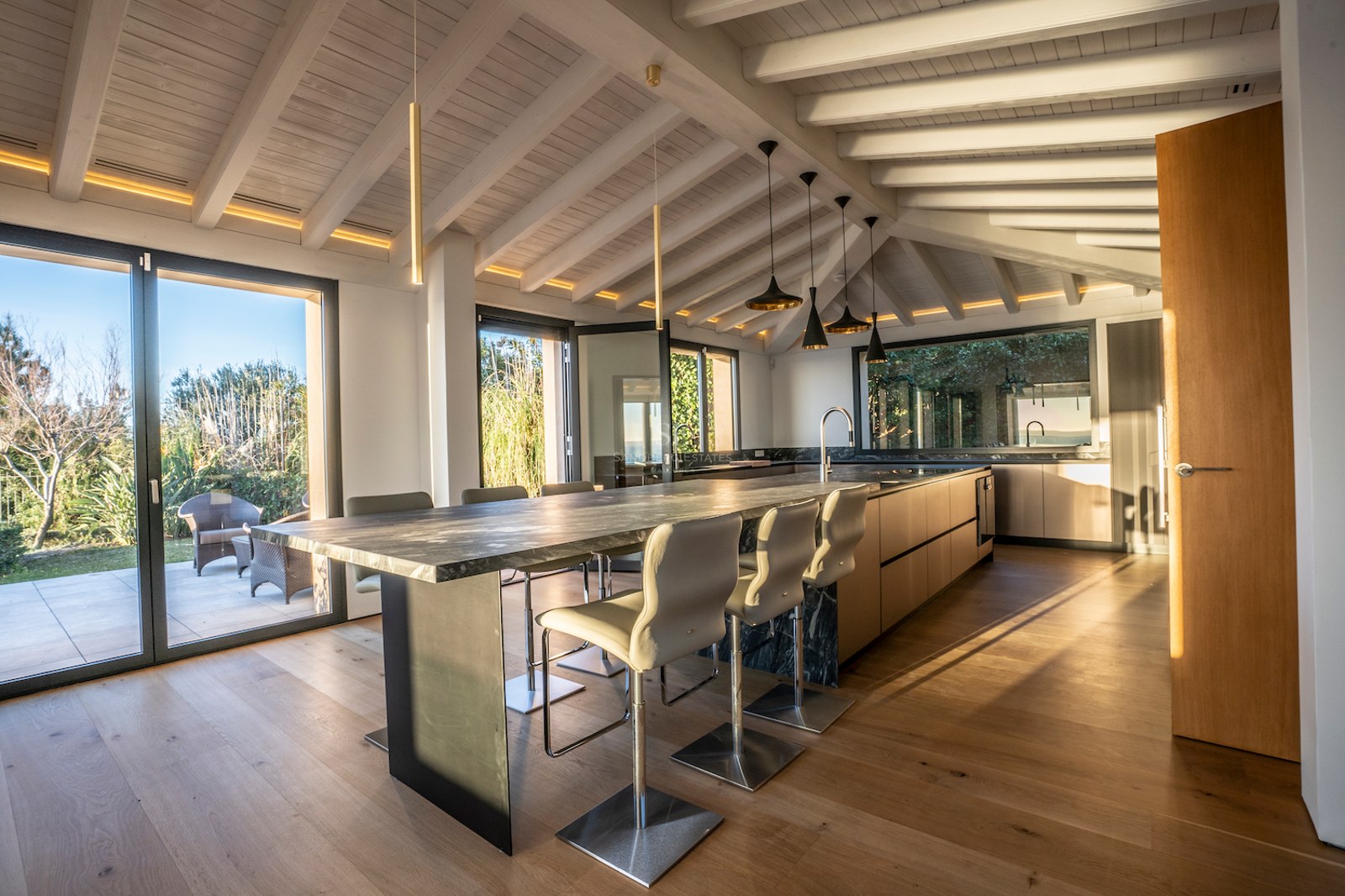 Contemporary kitchen featuring a dark marble island, white wooden beams, and floor-to-ceiling windows to the garden.