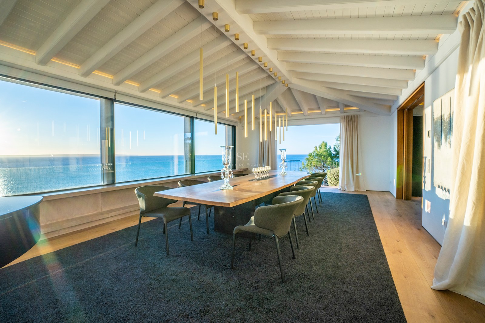 Luxury dining room featuring a solid wood table, designer seating, and expansive windows overlooking the Mediterranean Sea.
