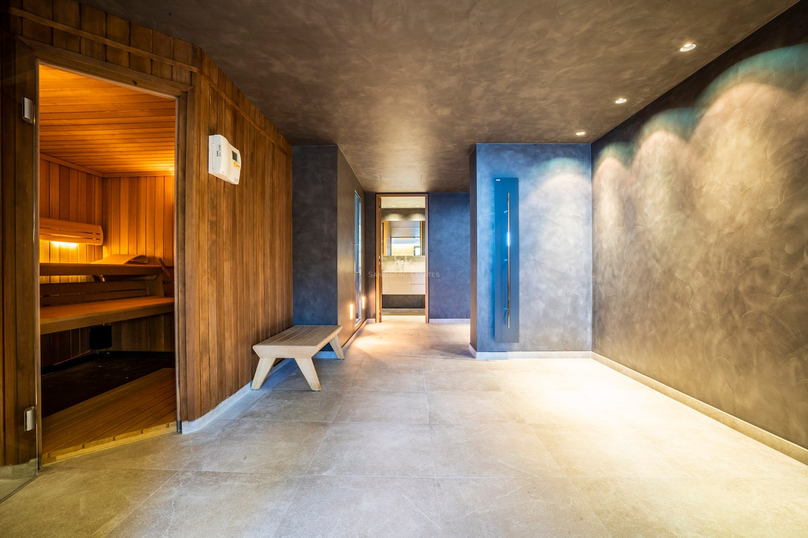 Modern indoor spa area with a wood-lined sauna, grey microcement walls, and large floor tiles under recessed lighting.