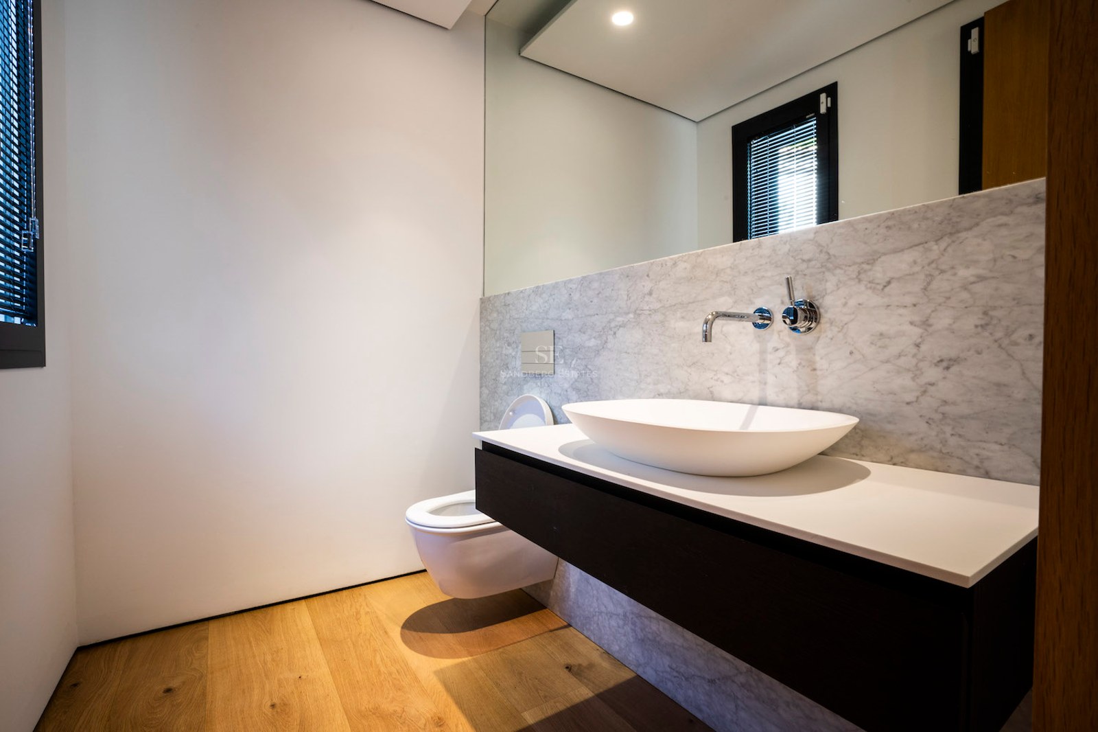 Contemporary bathroom featuring a white vessel sink on a floating vanity, stone wall tiles, and wooden flooring.