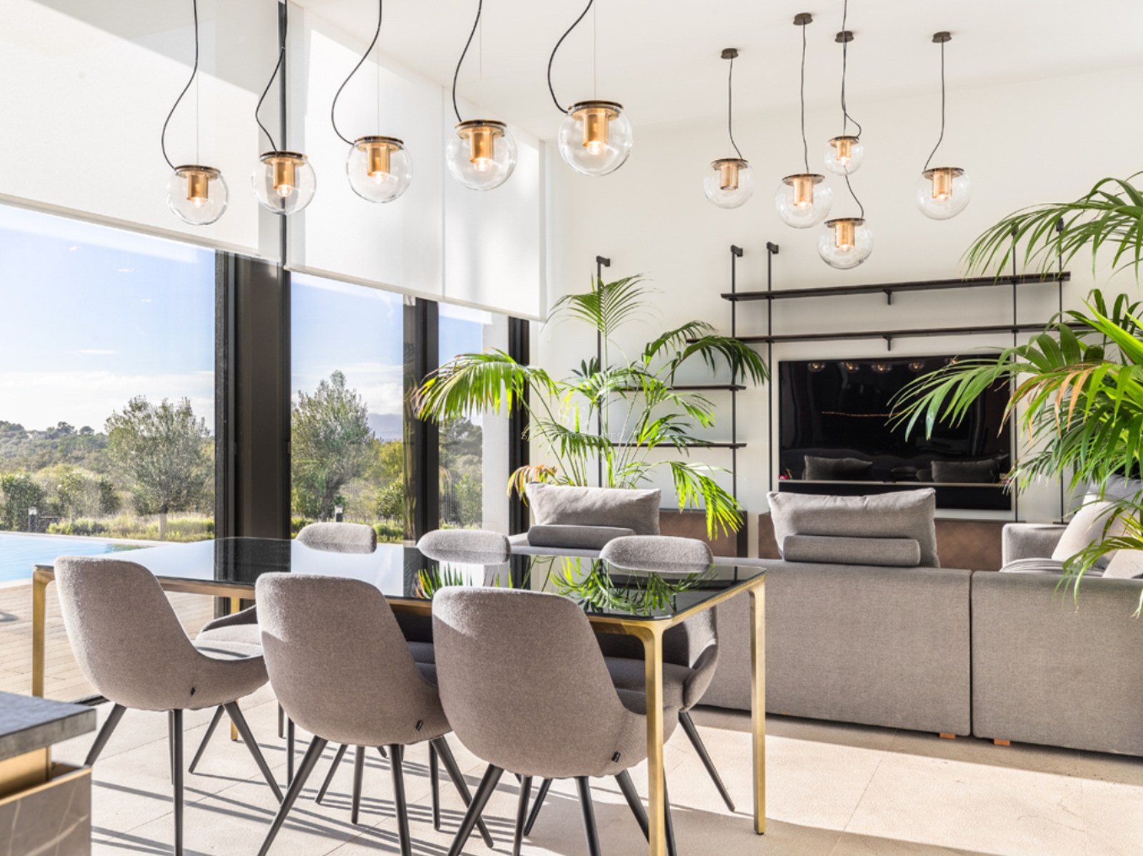 Salon et salle à manger modernes avec mobilier gris, suspensions design en verre et vue sur la piscine.